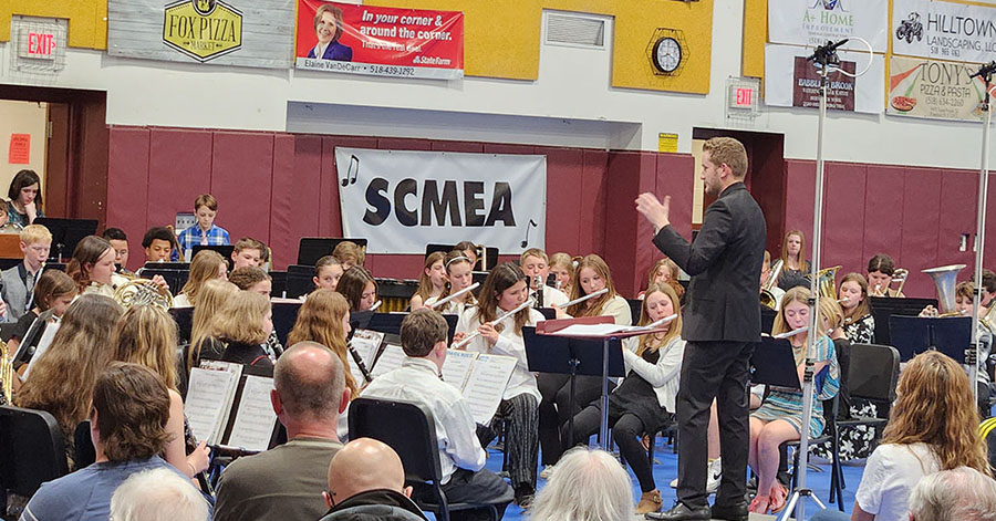 A crowd looks on as a conductor leads students in a musical performance.