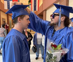Two students in cap and gown. One student is adjusting the tassel for the other student.