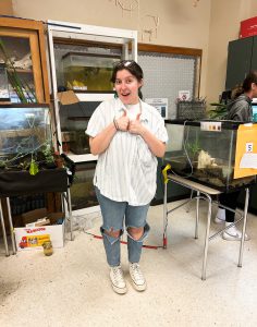 Teen gives the thumbs-up. She is standing next to an ecosystem display tank.