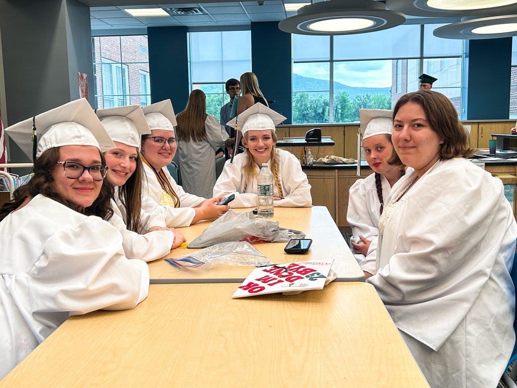Five students sit at table in cap and gowns