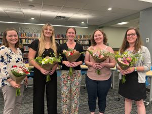 Five women stand together. Each is holding a bouquet.