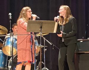 Student and teacher singing on stage together.