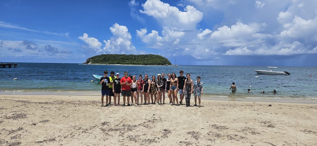 Students stand in a group at the beach.