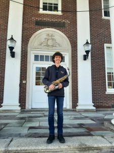 Matthew Quinn on steps of high school. He is holding a saxophone.