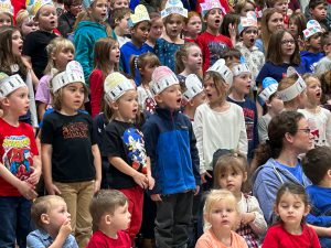 Children in hand-made hats singing.