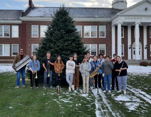 Students stand in front of holiday tree. They are holding instruments.