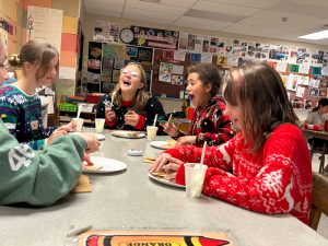 Five students work on gingerbread houses during art club. They are smiling and laughing.