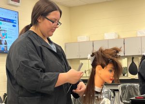 Erica Nahaczewski practices hair styling on a dummy.