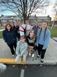 Eight students stand next to candy cane decoration in front of school