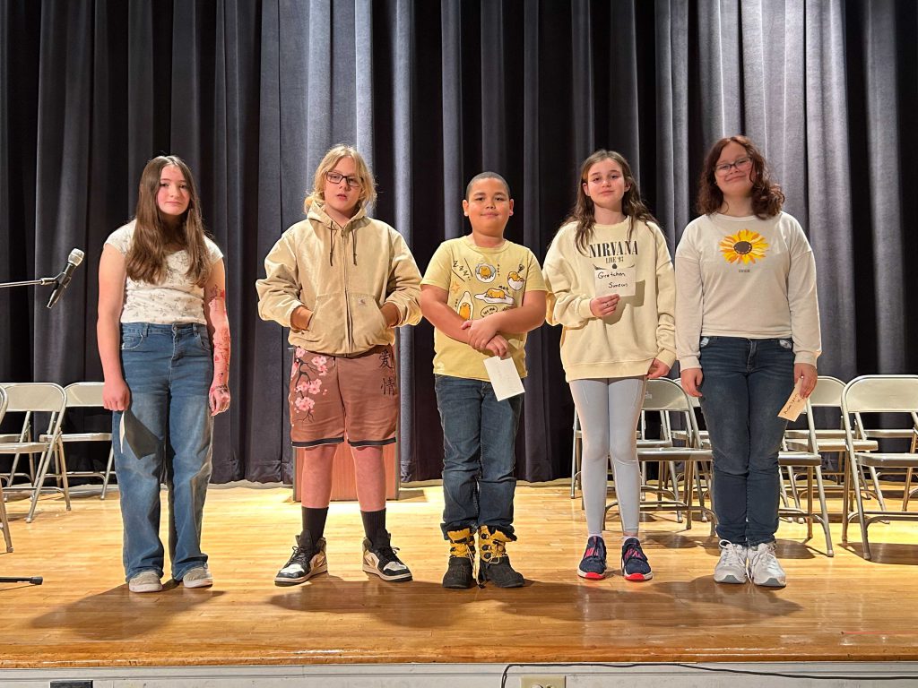 Five students stand on stage
