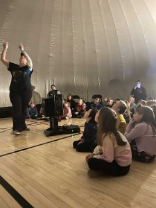 Instructor talks to students in planetarium.
