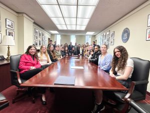 Students seated and standing in legislative conference room.