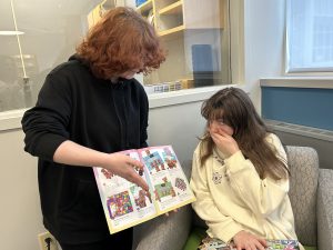 Student holds catalog of chocolates. Another student covers her mouth and looks upwards.