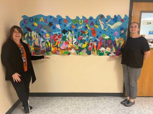 Two adults stand next to mural.