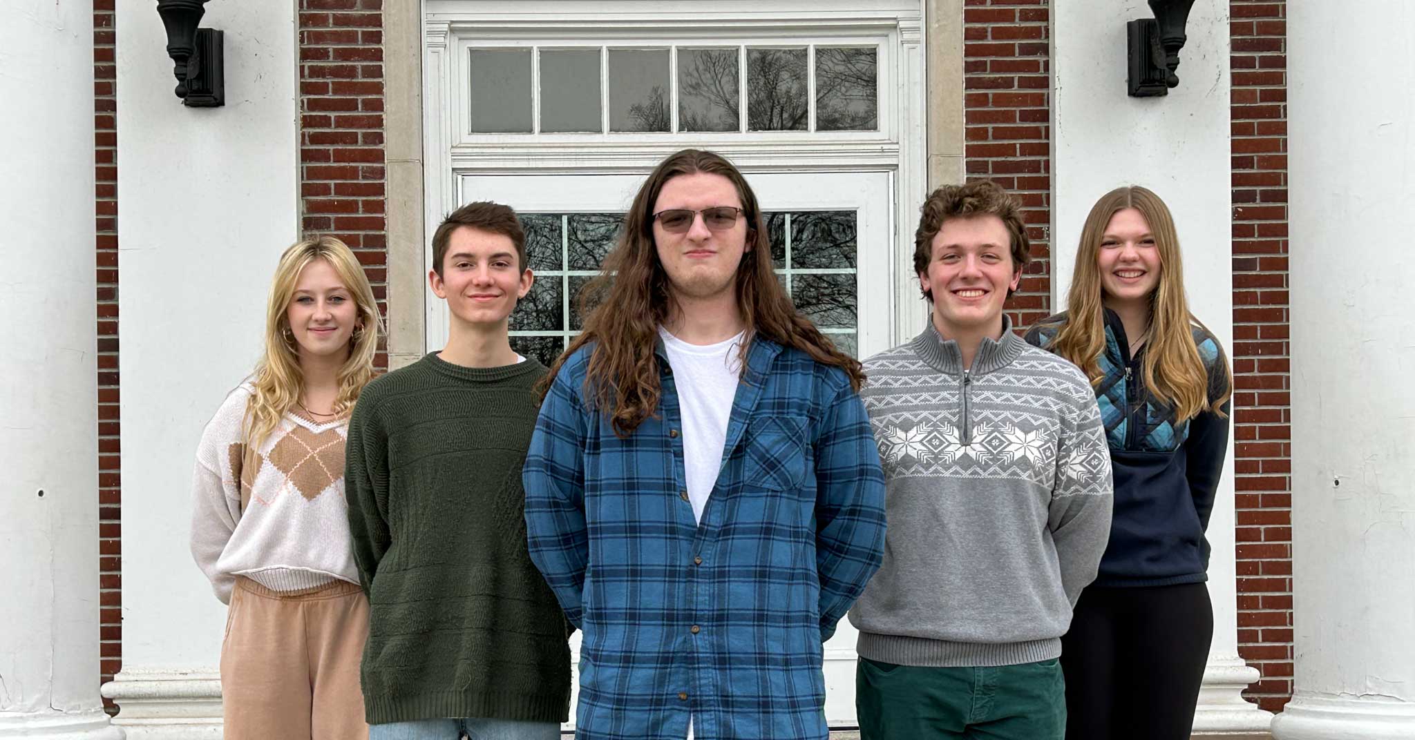 Five students standing in V formation on exterior stairs.