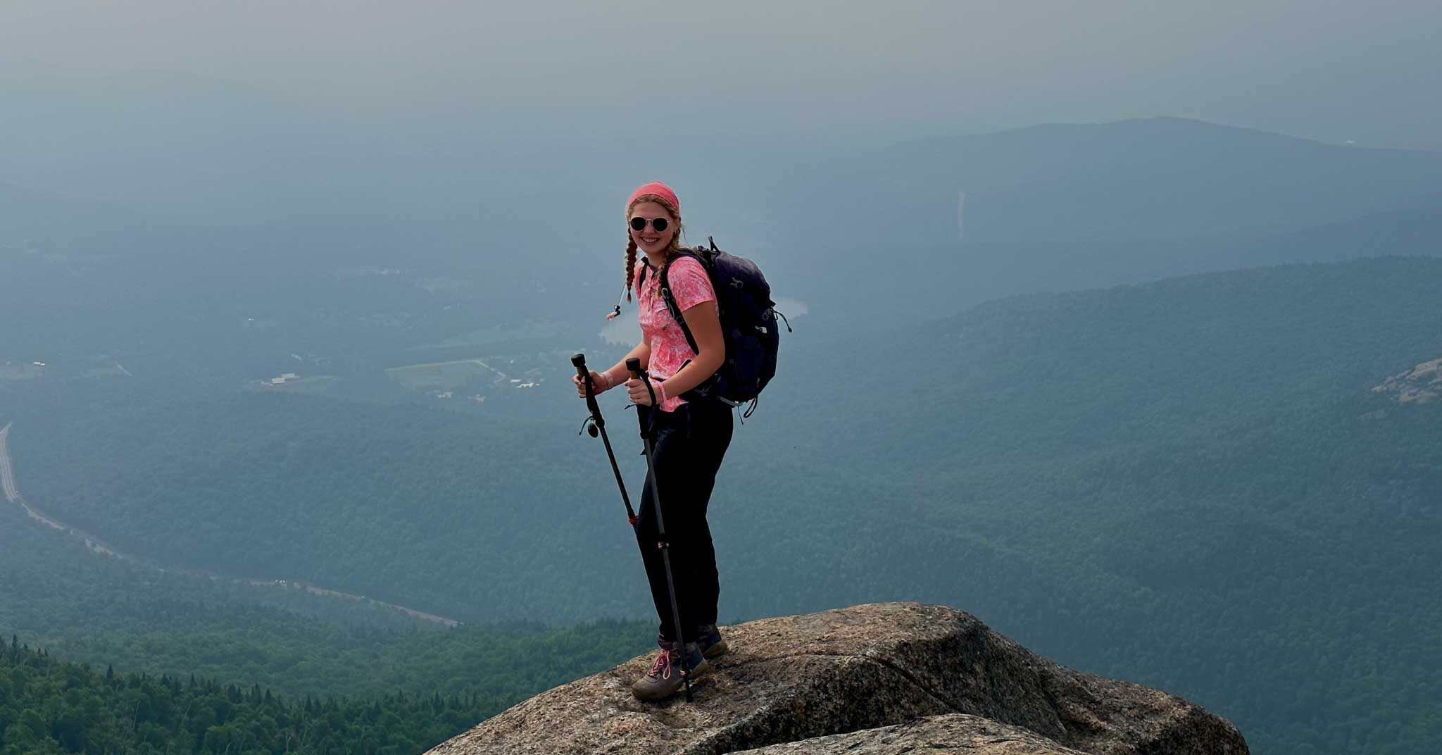 Teen hiker stands on top of mountain.