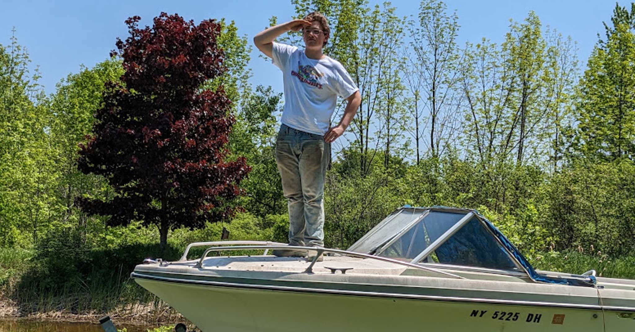 Teen stands with arm raised on hood of boat.