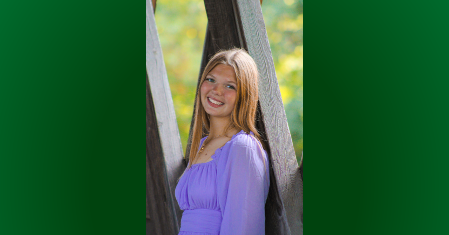 Teen stands against tree.