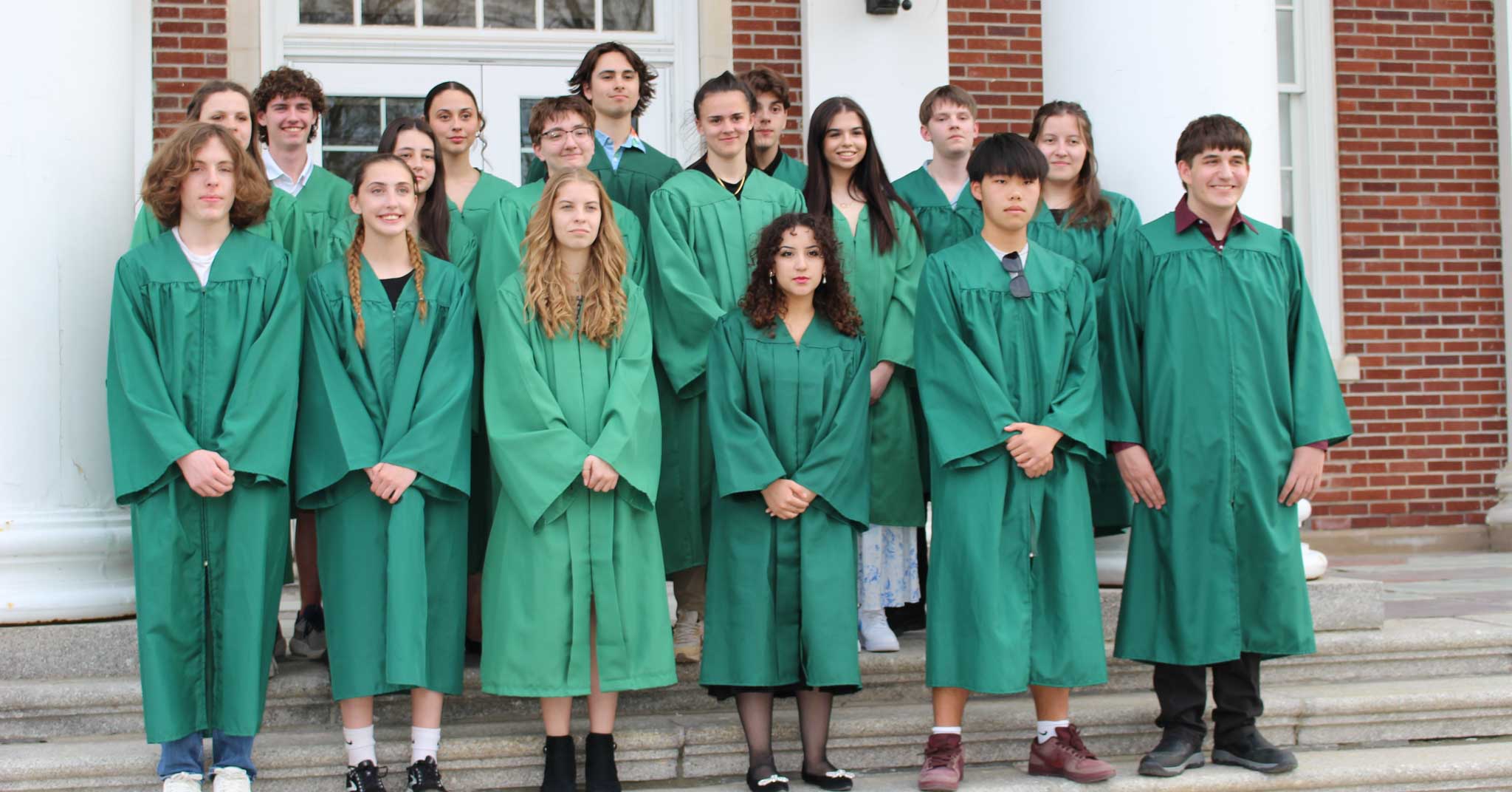 Members of the honor society stand on front steps of high school. They are wearing green robes.