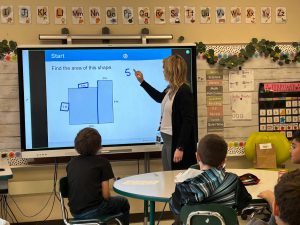 Teacher works on math problem in front of class.