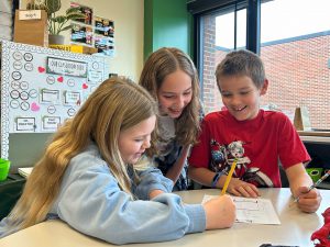 Three elementary students work on paper together.