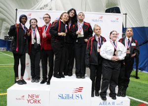 Group of award-winning students stand on stage of Skills USA platform.
