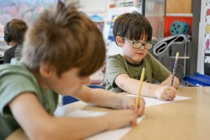 Two boys writing on paper with pencils.