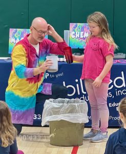 Adult in rainbow lab coat with a student.