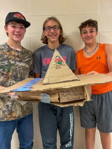 Three middle-school boys holds up a pyramid project.