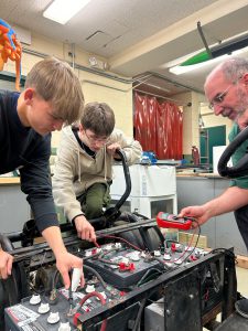 Teacher and two students work on a go-cart battery