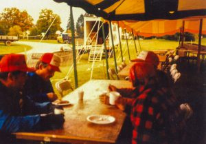 Community volunteers sit at a table with food under a tent.