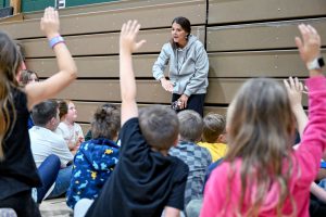 Students with raised hands look toward gym teacher.
