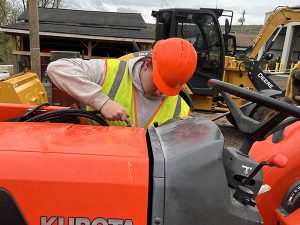 Teen, wearing safety garments, works on a tractor.