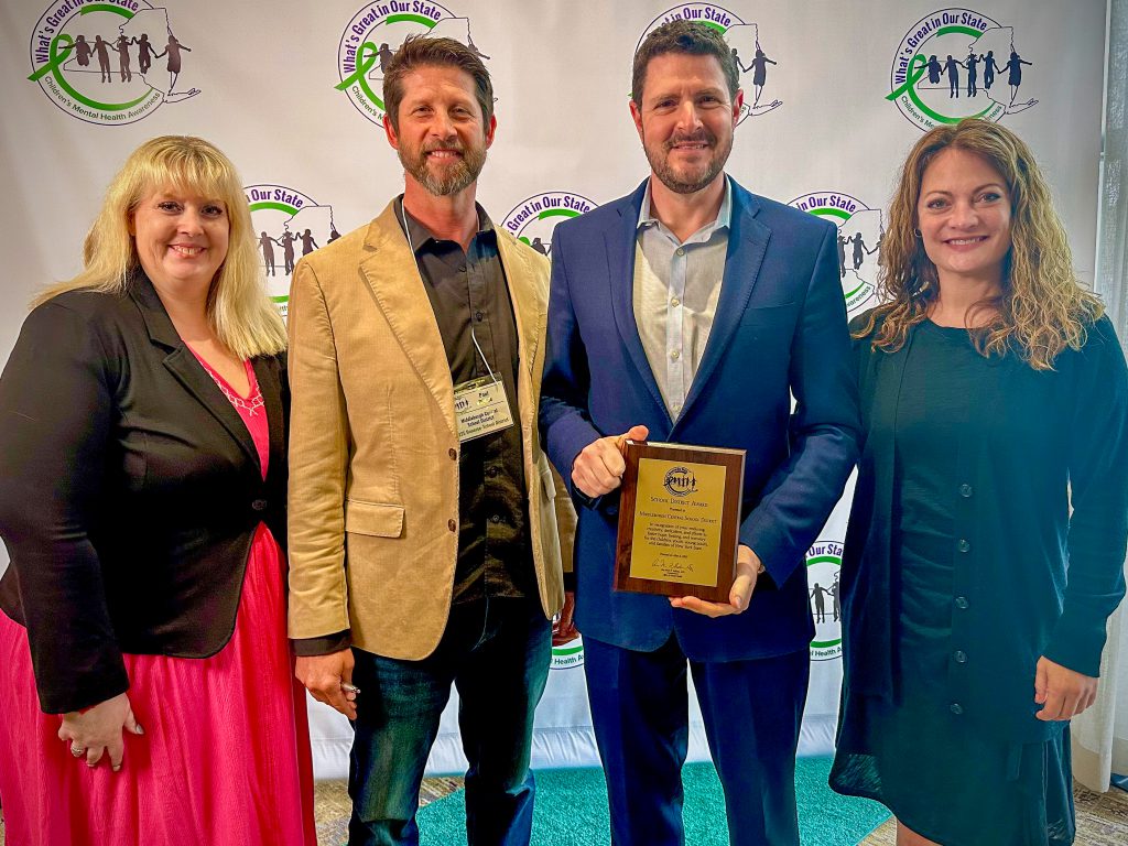 Four adults in professional attire. One is holding a plaque.