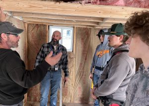Three teens and two teachers stand in unfinished building.