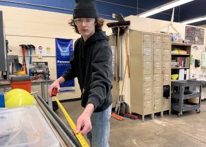 Student uses tape measure in large work shop.
