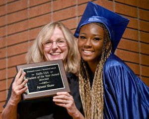 Adult holding award stands next to teen in cap and gown.