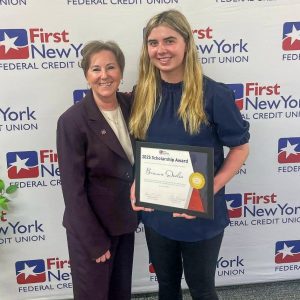Brianna Devlin holds certificate. She is standing next to an adult in front of First New York Federal Credit Union sign.