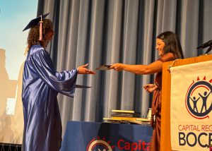Student, dressed in cap and gown, crosses stage to receive award.