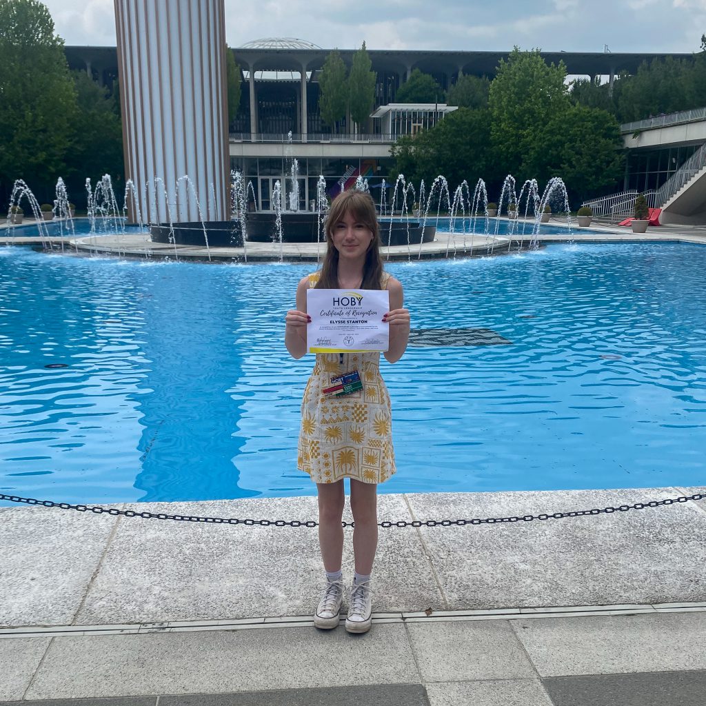 Elysse Stanton standing in front of fountains at University at Albany. She is holding a HOBY certificate.