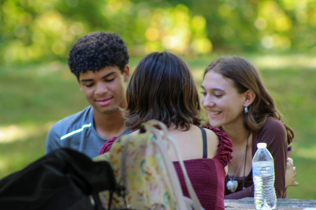 Three students sit at a picnic table in a park.