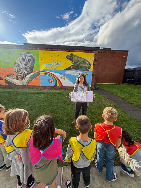Artist speaks to children. Mural in background.