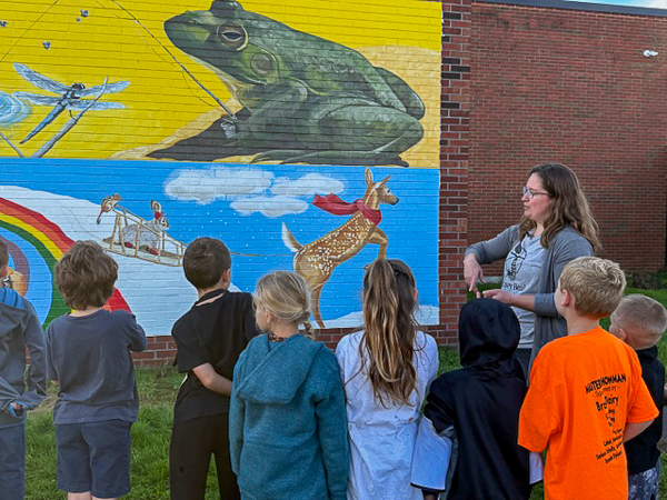 Artist speaks to children. Mural in background.