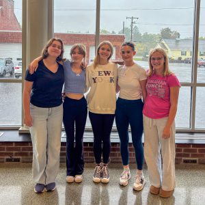Five students stand with arms around each other.