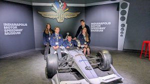 Five students wearing FFA jackets positioned on and around race car.