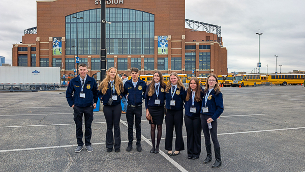 Teens in FFA jackets stand in a group outside stadium.