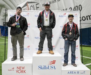 Three teens stand on a SkillsUSA podium with medals around their necks.