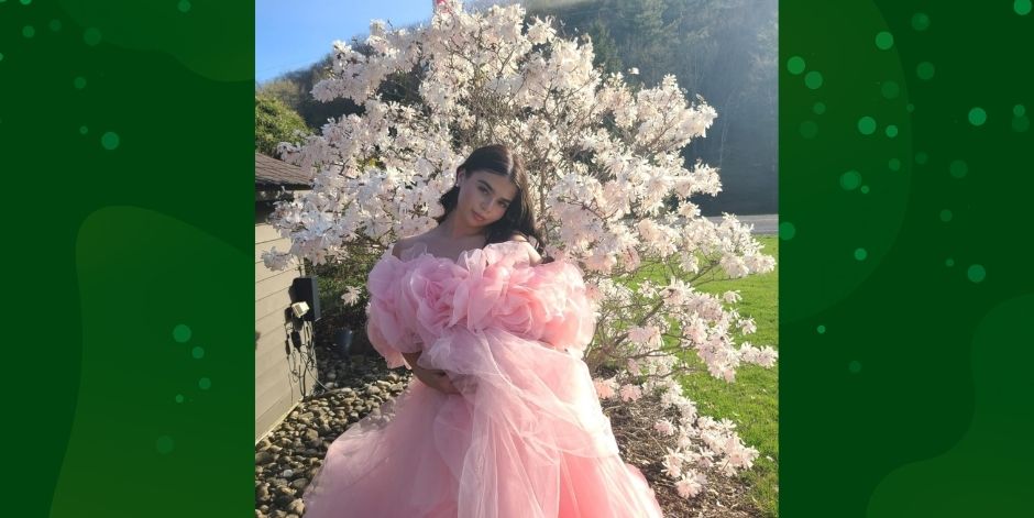 Teen, wearing flowing pink taffeta dress stands in front of a blossoming shrub.