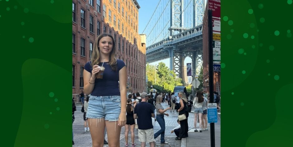 Student holds a drink on a crowded city street. Bridge in the background
