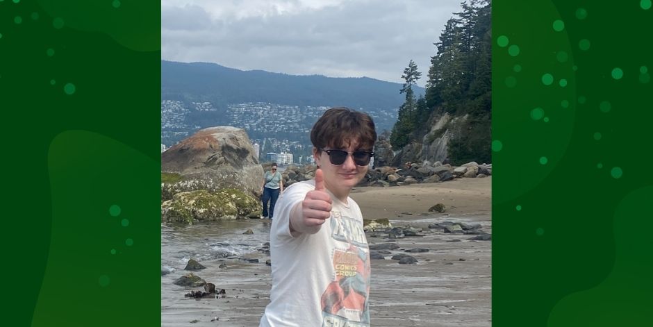 Teen wearing sunglasses gives the "thumbs-up" sign. Mountain in the distance.
